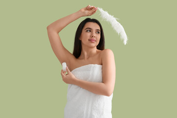 Wall Mural - Beautiful young woman in towel with crystal deodorant and feather on green background