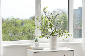 Vase with blooming branches on chest of drawers near window in room