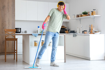 Wall Mural - Young man with headphones and mop listening to music in kitchen