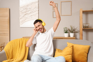 Canvas Print - Happy young bearded man in headphones listening to music on sofa at home