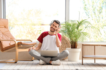 Sticker - Young bearded man in headphones with laptop listening to music on floor at home