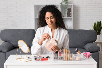 Wall Mural - Beautiful young happy African-American woman with cosmetic bag doing makeup at home