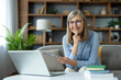 © Liubomir - Smiling senior woman working from home using a laptop and notebook. She is in a comfortable home office setting, representing remote work, education, and senior professional lifestyle.
