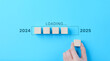 © Supatman - Loading Progress Bar from 2024 to 2025 with Wooden Blocks. A hand places wooden blocks in a row, creating a progress bar transitioning from 2024 to 2025, symbolizing the new year and future progress.