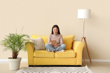 Wall Mural - Beautiful young woman reading book and sitting on yellow sofa at home