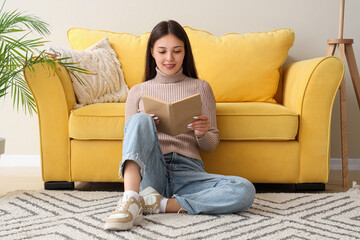 Wall Mural - Beautiful young woman reading book and sitting on floor at home