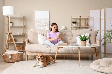 Wall Mural - Young woman reading book and cute Beagle dog lying on floor in living room