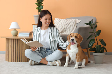 Wall Mural - Young woman reading book with adorable Beagle dog resting on floor in living room