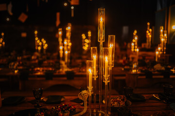 Dobele, Latvia - June 7, 2024 - Elegant candlelit dinner setting with tall glass candlesticks creating a warm and intimate ambiance. Blurred background with dining tables. Copy space.