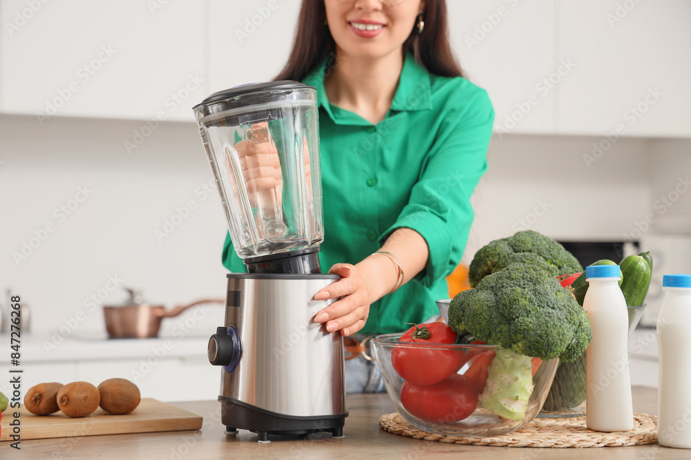 Young woman with blender at table in kitchen, closeup