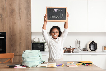 Canvas Print - Little African-American schoolgirl holding chalkboard with text I LOVE HOMEWORK in kitchen