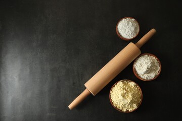 Wall Mural - Rolling pin and different types of flour on black table, flat lay. Space for text