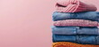 © Anna - A stack of folded sweaters and blue jeans on a pink background. Banner for washing, ironing, soft clothes, conditioner or laundry powder