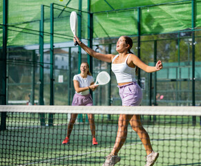 Wall Mural - Young woman in shorts jumping while playing padel tennis on court. Racket sport training outdoors.