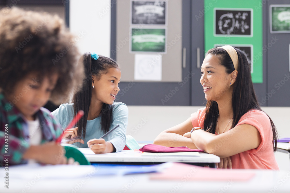 Biracial female teacher interacting with two students in classroom ...