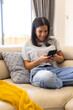 © Wavebreak Media - Biracial young woman sitting on couch looking at her smartphone and smiling, at home