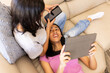 © Wavebreak Media - Two young biracial friends relax on a couch, one with a smartphone and the other a tablet, at home