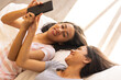 © Wavebreak Media - Two young biracial sisters lie on a bed, smiling and sharing a moment with a phone, at home