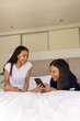 © Wavebreak Media - Two young biracial friends are looking at smartphone and smiling, at home