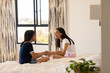 © Wavebreak Media - Two young biracial friends are sitting on bed, smiling and holding hands, at home