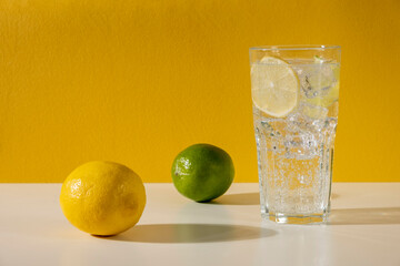 Wall Mural - Glass ice lemonade on yellow background. Minimal style composition summer drink.