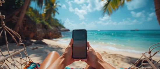hands using smart phone with blank screen, on the beach while sitting in a hammock, mobile phone and