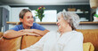 © AchillesReel/peopleimages.com - Senior, woman and happy with caregiver for support in nursing home for assistance, gratitude and service. Elderly patient, nurse and smile on sofa for helping hand, conversation and help in hospice