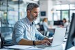 © WMSTUDIO - A dedicated professional at their workstation, typing on a laptop and referencing documents. The bright office environment promotes focus and creativity with its clean design.