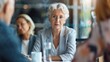 © Denisa - A woman with white hair and glasses listens intently to her colleagues during a meeting
