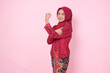© Reezky - Confident Asian woman wearing modern kebaya dress and hijab showing strong gesture by lifting her arms and muscles over isolated pink background.