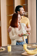 Wall Mural - A beautiful adult couple, a redhead woman and a bearded man, standing next to each other in a modern kitchen.