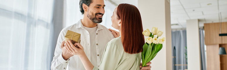 Wall Mural - A bearded man in a modern apartment offers a bouquet of flowers to his redhead woman, creating a sweet and romantic moment.