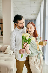 Wall Mural - A redhead woman and bearded man hold flowers in a modern living room, enjoying quality time together.
