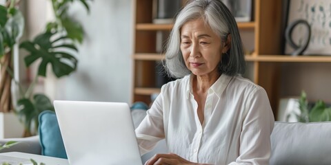 Elderly Chinese woman using a laptop at home, highlighting technology and senior lifestyle.