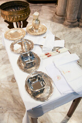 Silver and gold religious items set up on a table with white cloth for a baptism ceremony