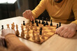 © mtrlin - Close-up view of two men playing chess at home. The focus is on their hands and the wooden chessboard as they make strategic moves in an indoor setting. Hobby and leisure