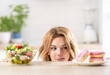 © weyo - Beautiful young woman tempted having to make choice between fresh lettuce salad and doughnut in healthy unhealthy food, detox eating, calories and diet concept.