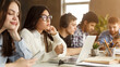 © Prostock-studio - A collection of multiethnic students is deeply focused on their individual studies at a long table basked in sunlight. With books open and laptops out, they sit intently working, some writing notes