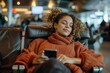 © Pinklife - Content young woman with curly hair relaxing while listening to music on her phone at an airport lounge
