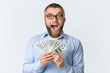 © Prostock-studio - A man wearing a blue shirt is holding a stack of money in his hand. He looks at the money while standing in a room with neutral background.