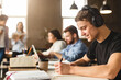 © Prostock-studio - Student guy preparing for classes, taking notes in university library, listening music in headphones