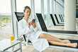 © LIGHTFIELD STUDIOS - A young brunette woman in a bathrobe relaxes in an indoor spa while using a cell phone.