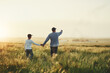 © Stratford/peopleimages.com - Back, field and father with son, holding hands and walking with sunshine, travel and bonding together. Family, single parent and dad with kid, boy and child with weekend break, nature and adventure