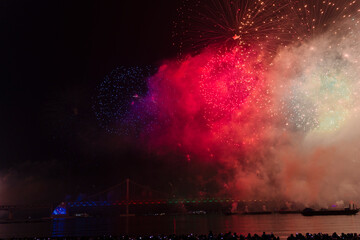  a vibrant fireworks display over a bridge at night in Busan, Korea, with spectators silhouetted against the illuminated sky.