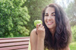 © Анна Демидова - Young woman with a green apple in a summer park on a sunny day. A beautiful smiling brunette in a yellow top is sitting on a bench. Healthy organic products. Close-up.