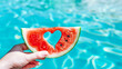 © Creativision - hand holding a watermelon slice with a heart inside at summer pool background