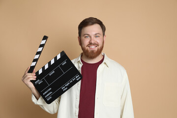 Poster - Making movie. Smiling man with clapperboard on beige background