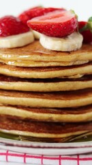 Wall Mural - Stack of pancakes with maple syrup, bananas, and strawberries. Close-up. Vertical video. Healthy dessert or sweet breakfast food.