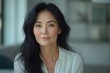 © Aaron Weiss - A woman with long black hair and a white shirt is sitting in a room. She has a serious expression on her face