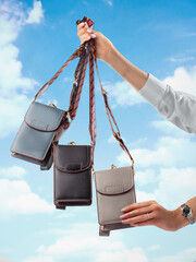 Wall Mural - Collection of stylish designer leather crossbody bags with decorative ethnic patterned straps, presented in female hands against clear blue sky backdrop. Craft accessory for daily use